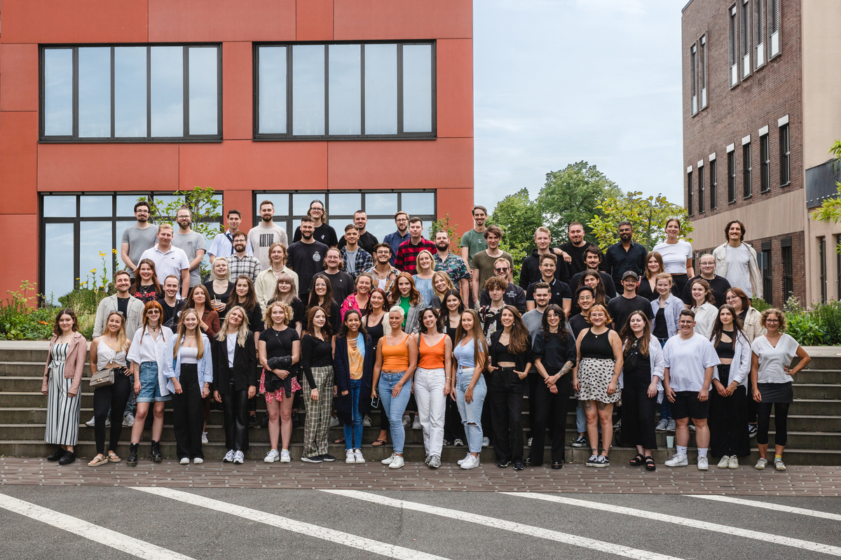 Große Gruppe vor einem roten Bürogebäude.