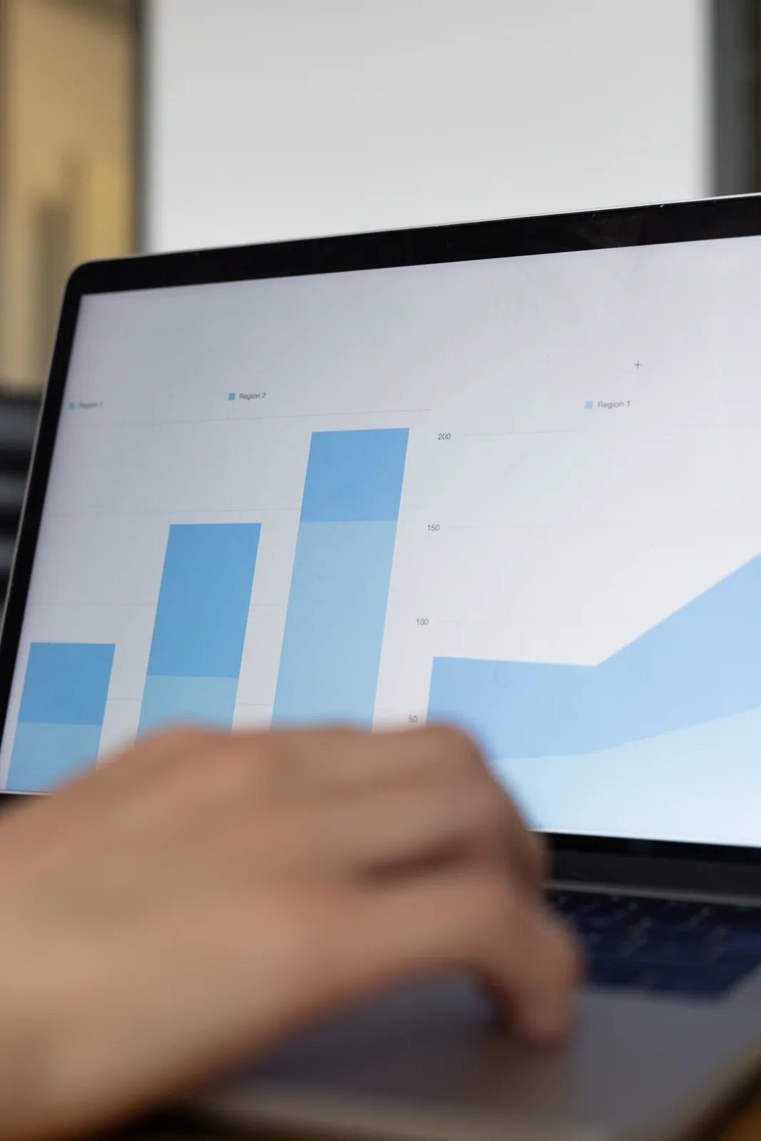Blaue Balken- und Flächendiagramme auf einem Laptop mit einer Hand im Vordergrund.