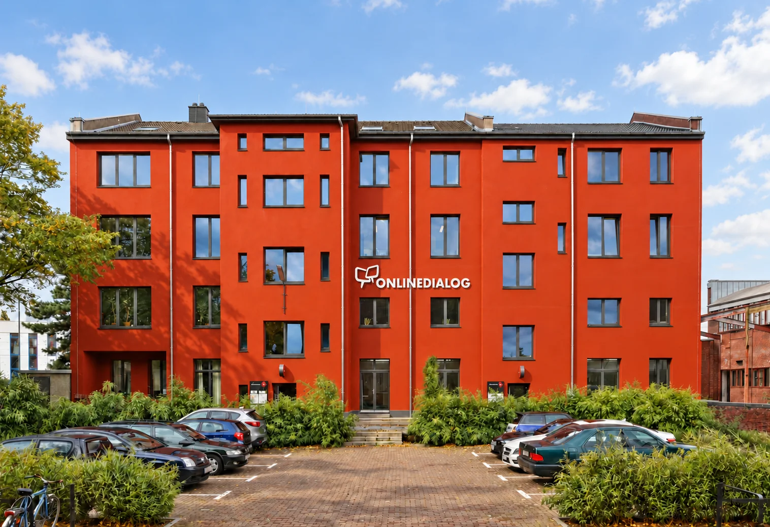 Das Atelierhaus im Kreativareal Schwanenhöfe in Düsseldorf – mit visualisiertem weißem OnlineDialog-Logo und sonniger Lichtstimmung